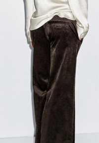 Brązowe szerokie spodnie z korduroy z pionowymi prążkami, z wysokim stanem i bocznymi kieszeniami, noszone z jasnym satynowym topem.