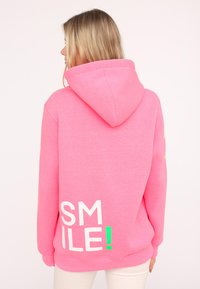 Rosa Kapuzenpullover mit weißem und neon-grünem "SMILE!"-Text auf dem Rücken. Weicher Stoff, lockere Passform und große Kapuze.