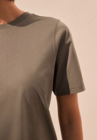 T-shirt grigia a maniche corte in tessuto morbido, con classico scollo a girocollo e dettagli di cuciture sottili sulle spalle.