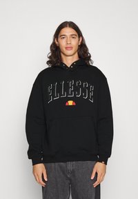 Zwarte hoodie met een logo waarop "Ellesse" prominent in een groot, vet lettertype staat. Bevat een voorzak en een verstelbare capuchon met metalen details.