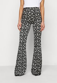 Svängda byxor i svart med ett vitt blommönster. Hög midja, slät textur och en avslappnad passform som sträcker sig ner till anklarna.