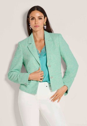 Mintgrüner Tweed-Blazer mit strukturierter Form, zwei Knöpfen und texturiertem Stoff. Getragen über einem petrolfarbenen Spitzentop und weißen Hosen.