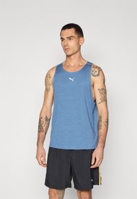 Blå ærmeløs tanktop lavet af et textured stof, med et hvidt logo på brystet, parret med sorte shorts.