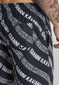 Crne hlače s bijelim tiskanim logotipom, s elastičnom waistbandom, bočnim džepom i glatkom teksturom tkanine.