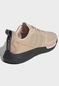 Beige mesh sneaker with three tonal stripes, pink accents, and black sole. Features a textured overlay and a branded heel tab.