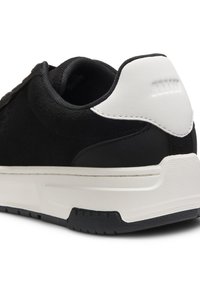 Μαύρο αθλητικό παπούτσι με επάνω μέρος από σουέτ, λευκή λεπτομέρεια στη φτέρνα, υφασμένη σόλα και επίπεδα κορδόνια. Διαθέτει επένδυση στον αστράγαλο για άνεση και στήριξη.