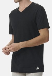 Svart bomulls T-shirt med V-hals, korta ärmar och en vit Adidas-logotyp i nedre högra hörnet. Slät textur.