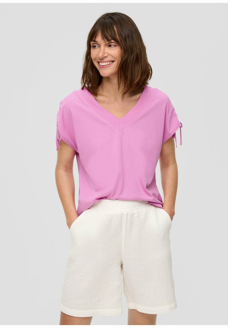 Pink V-neck short-sleeve top with drawstring details, paired with textured white shorts featuring an elastic waistband and side pockets.