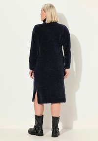Abito a maglia blu navy con collo alto, maniche lunghe e fessure laterali. Realizzato in materiale morbido, presenta una finitura calda e texturizzata.