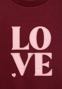 Burgunderfarbenes Sweatshirt mit großen, pinken, gestickten Buchstaben, die "LIEBE" spelllen, sowie einer kleinen Herzdetails unter dem Text. Weicher Stoff.