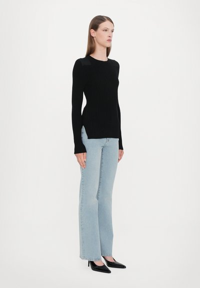 Black ribbed long-sleeve top with side slits, paired with light blue flared jeans and black pointed-toe heels. Simple, modern silhouette.