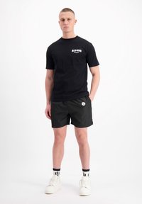 Zwart katoenen T-shirt met wit logo, gecombineerd met zwarte shorts en witte sneakers. De sokken zijn zwart met witte accenten en logo's.
