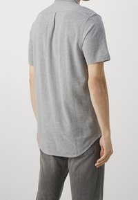 Polo grigio a maniche corte con una texture morbida, dotato di colletto, pieghe posteriori e orlo curvo, abbinato a pantaloni grigi.