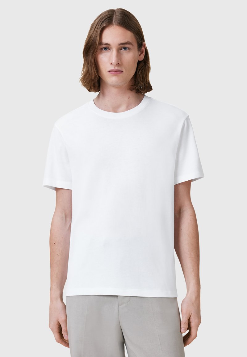 T-shirt bianco in cotone con scollo rotondo e maniche corte, caratterizzato da una vestibilità rilassata. Il tessuto appare morbido e leggero.