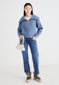 Lys blå ribbestrikket genser med overdimensjonert krage, glidelåslukking, parret med blå denim jeans og metallisk-brune plattformstøvler.