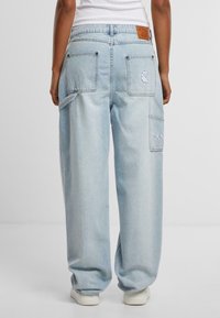 Pantaloni cargo in denim azzurro chiaro con vestibilità rilassata, numerose tasche e un'etichetta in pelle in vita. Texture morbida, design a gamba dritta.