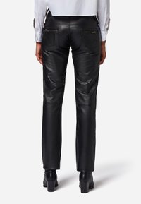 Svarta läderbyxor med smal passform, bakfickor med zippers, slät textur och minimalistisk design. Bärs med svarta klackstövlar.