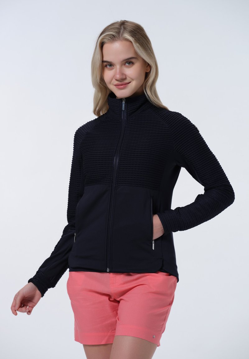 Svart zip-up jacka med texturerad ribbad design på axlar och armar, i kombination med ljusrosa shorts som har sidofickor.