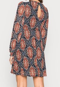 Mörkblå långärmad klänning med mönster i orange och vitt paisleymönster, detalj med nyckelhål i ryggen, följsam design och mjuk tygtextur.