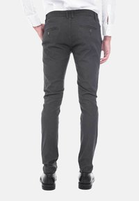Pantaloni slim-fit grigi a fantasia con due tasche posteriori e una texture liscia, indossati con una camicia bianca a maniche lunghe e scarpe nere.