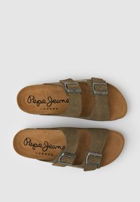 Brūni zamšāda sandaļi ar diviem regulējamiem sprādzes siksnām, mīkstu gaiši brūnu pēdu daļu un melnu zoli. Redzama "Pepe Jeans London" zīmola nosaukums.
