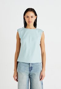 Top sans manches bleu clair avec une coupe carrée et un design aux épaules larges, fabriqué en tissu doux ; associé à un jean en denim délavé, à coupe ample.