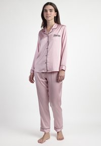 Conjunto de pijama de satén rosa que incluye una camisa de botones de manga larga con ribete negro y un logo bordado de "Barbie", acompañado de pantalones a juego.