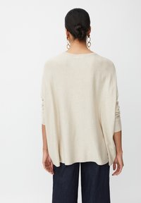 Beiger Strickpullover mit lockerer Passform, überschnittenen Schultern und langen Ärmeln. Weiche Textur. Tragen mit dunklen, weiten Hosen.