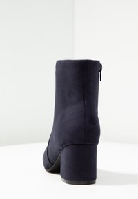 Bottine en suédine synthétique bleu marine avec un talon carré haut, une texture lisse et une fermeture éclair au dos pour un enfilage facile.