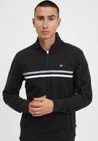 Black zip-up sweatshirt with a high collar, featuring two horizontal stripes in gray and white across the chest. Soft texture, side pockets.