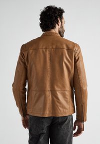 Brun læderjakke med et klassisk design, der har lynlåslukning, lodrette sømme og en skræddersyet pasform. Forstærkede sømme og sidelommer.