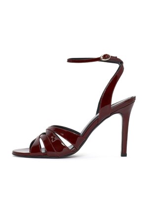Bordeaux lakleren sandaal met hoge hak, enkelriem met gesp en meerdere voorste banden, zijaanzicht op witte achtergrond.