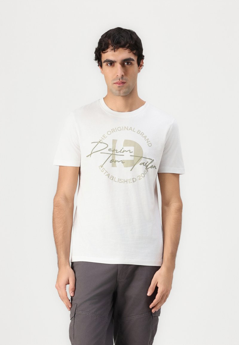 Hvit bomulls T-skjorte med rund hals og korte ermer. Sentral grafikk i beige med tekst "THE ORIGINAL BRAND" og "Denim."
