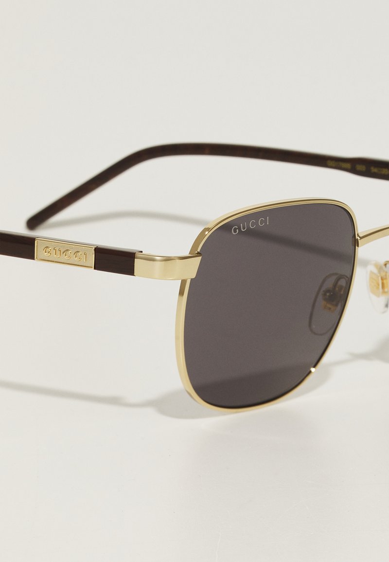 Lunettes de soleil rectangulaires avec des verres teintés, monture en métal doré et branches en acétate marron. Présente le logo de la marque sur les branches.