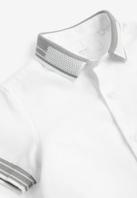 Polo blanc avec col texturé gris et blanc et poignets rayés gris, boutonné à l'avant.