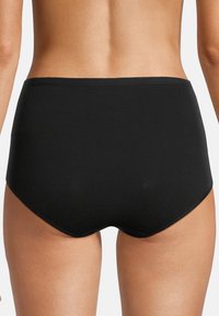 Persona che indossa slip neri a vita alta, mostrata di spalle, su uno sfondo bianco semplice.