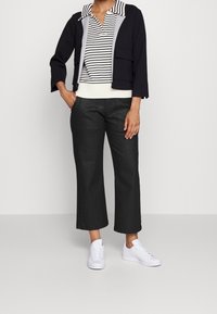 Chaqueta corta navy con forro gris, polo a rayas en blanco y negro, y pantalones de pierna ancha en gris oscuro; zapatillas blancas completan el look.