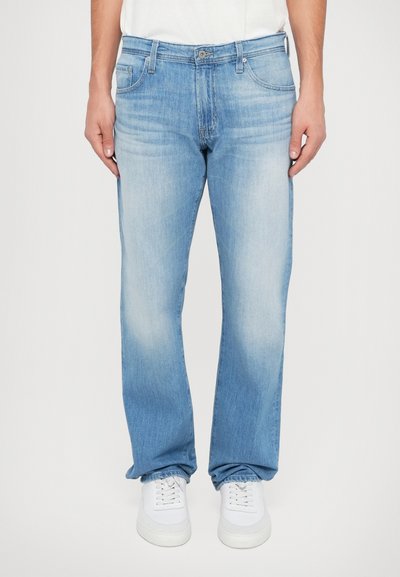 Jean en denim bleu clair avec une coupe ample, présentant des dégradés subtils et un design classique à cinq poches, accompagnés de baskets blanches.