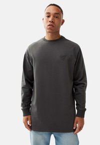 Dark gray sweatshirt with long sleeves, made of cotton. Features a round neck and a small embroidered logo on the chest.