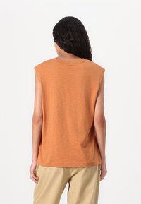 Haut en coton orange sans manches avec un col rond et une coupe décontractée, présentant une texture subtile et un ourlet droit.