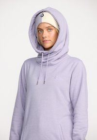 Sweatshirt lilas clair avec une grande capuche ample, des cordons de serrage et un logo brodé sur la poitrine. Texture de tissu douce.