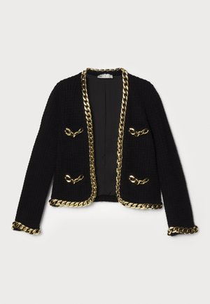 Veste noire texturée avec des bordures en chaîne dorée le long des bords et des poches, et des accents en quincaillerie décoratifs à l'avant.