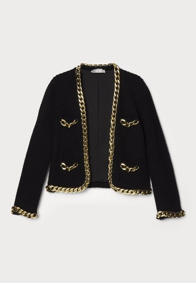 Czarna kurtka o teksturowanej fakturze z złotym łańcuchem wzdłuż krawędzi i kieszeni, z dekoracyjnymi elementami metalowymi na przodzie.