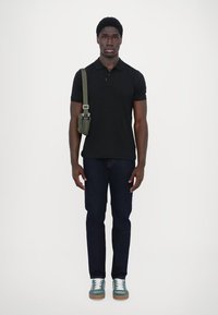 Čierna polo tričko, tmavé rifle, zelené tenisky a malá zelená crossbody taška. Jednoduchý dizajn s krátkymi rukávmi a klasickým golierom.