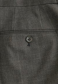 Pantalon habillé en tissu à carreaux gris, doté d'une poche arrière unique avec fermeture à bouton gris et de détails subtils en tissu texturé.