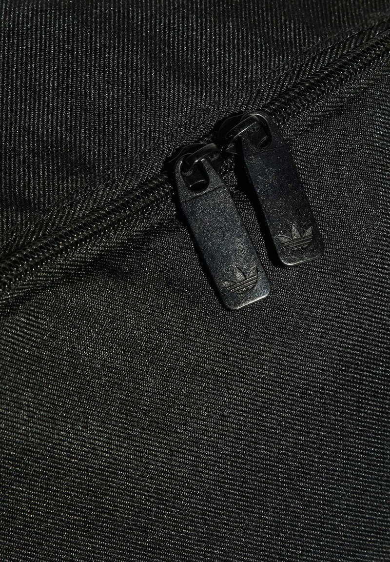 Pochette noire en tissu dotée de deux zips métalliques avec étiquettes de logo. Le matériau a une apparence texturée.