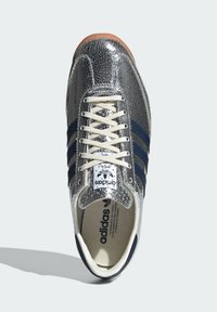 Baskets en cuir argent craquelé avec des rayures bleu marine, des lacets crème et une semelle en gomme texturée. Comprend un logo Adidas sur la languette.