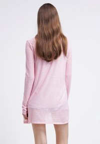 Långärmad, ljusrosa topp i transparent tyg. Har en avkopplad passform med en något längre bakre fåll. Minimal detaljer, jämn textur.