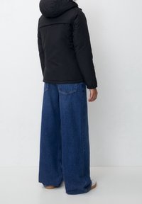 Sort puffersjakke med hætte, parret med løse, vide mørkeblå jeans. Outfittet har en struktureret overflade og en enkel design.