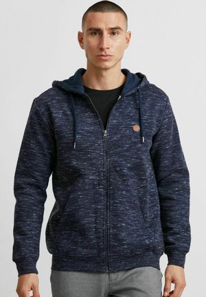 Sudadera navy con un patrón texturizado, cierre de cremallera, bolsillos delanteros y una capucha interior de contraste. Acentuada con un pequeño parche de logo.